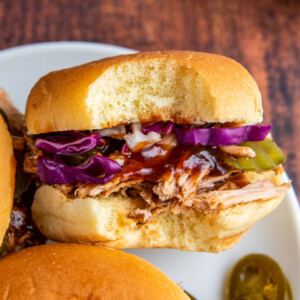 Pulled pork sandwich with bbq sauce, pickles and cabbage and a bite taken out of it.