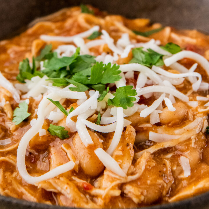 Up close image of white chicken chili in a brown bowl with cheese and cilantro on top.