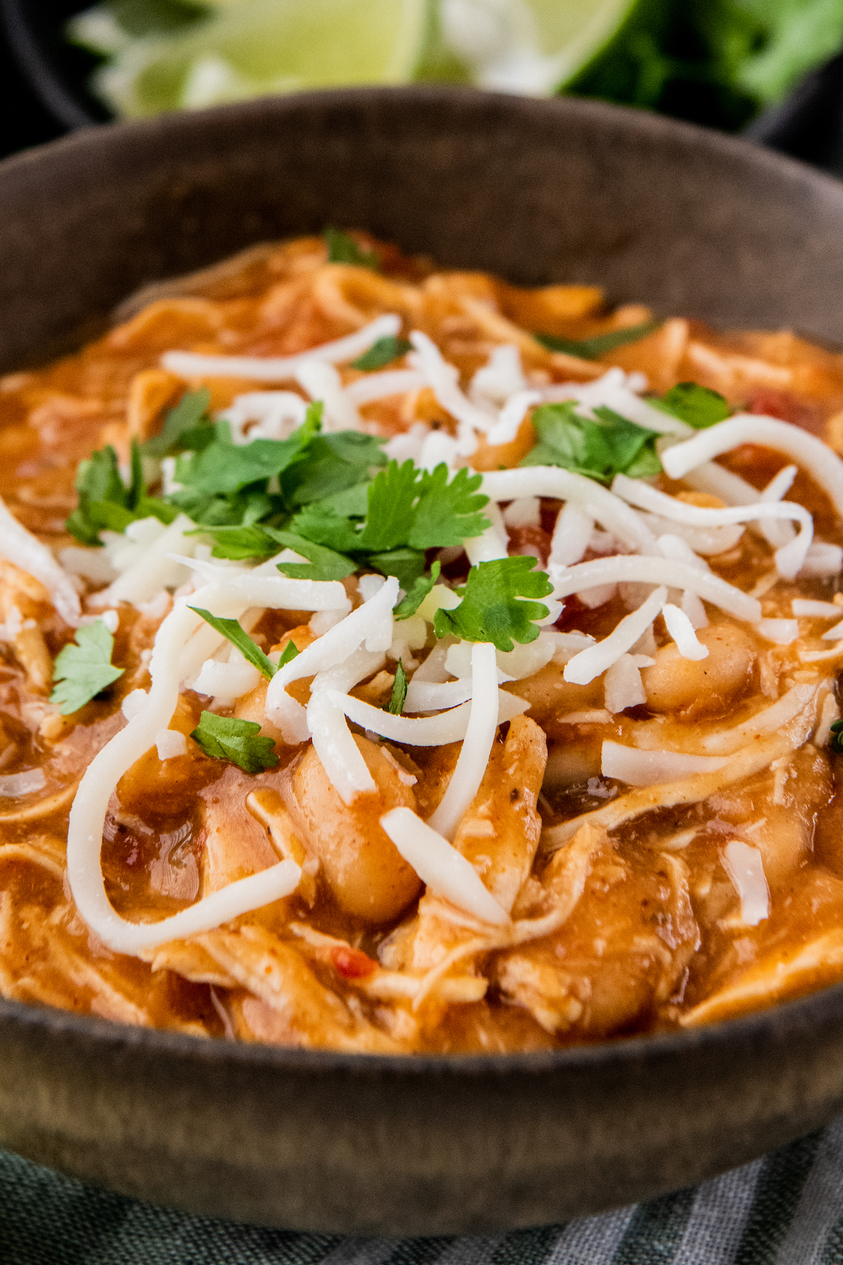 Up close image of white chicken chili in a brown bowl with cheese and cilantro on top.