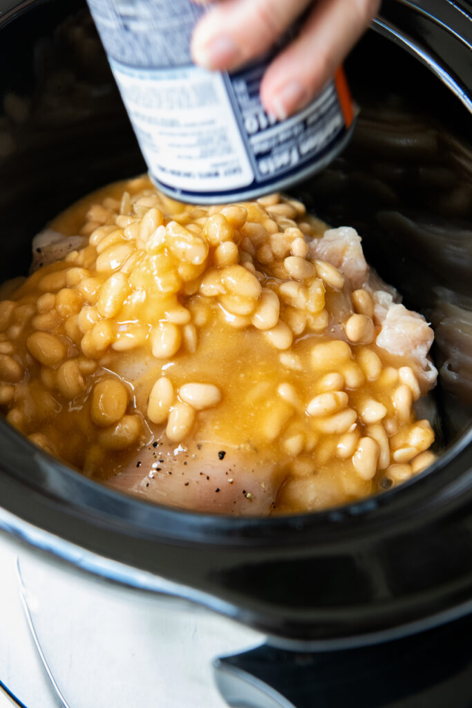 Canned white beans being poured into a crockpot bowl.