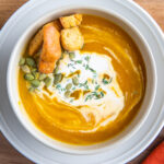 A bowl of butternut squash soup with cream on top and a fall napkin.