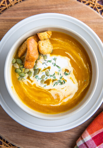 A bowl of butternut squash soup with cream on top and a fall napkin.