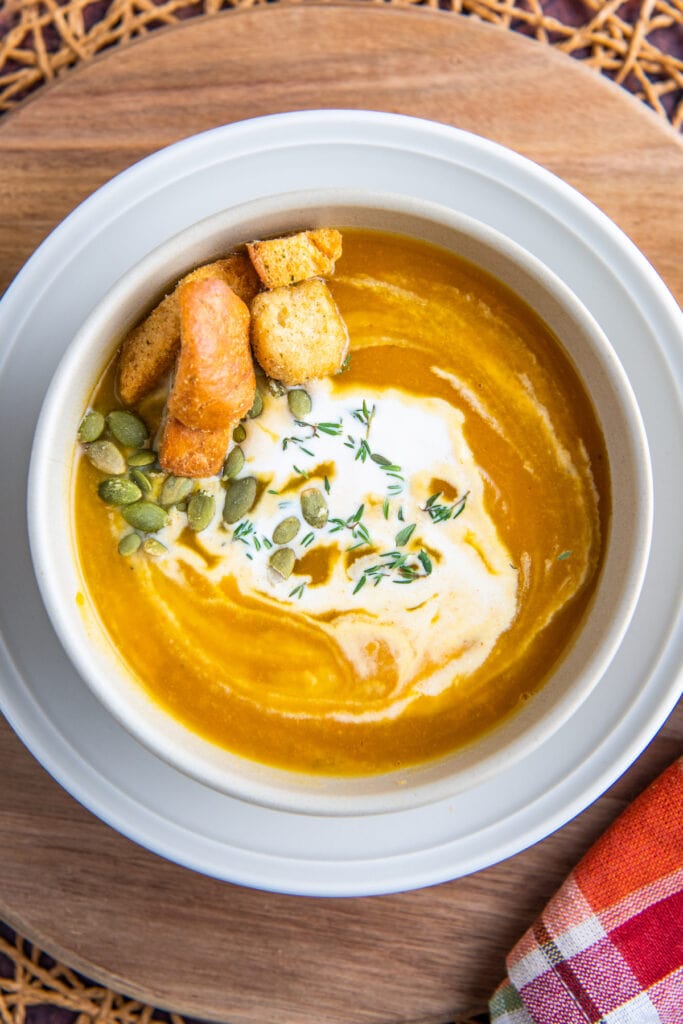 A bowl of butternut squash soup with cream on top and a fall napkin.