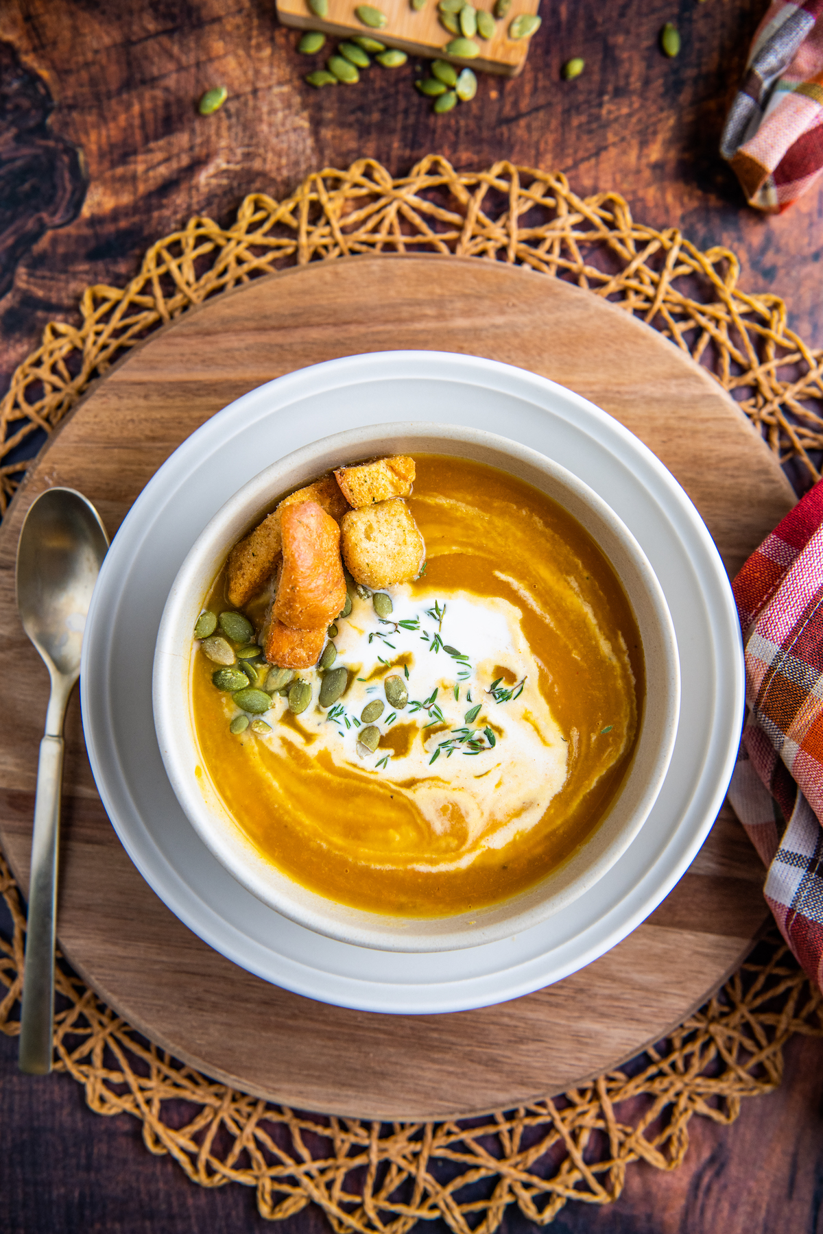 A bowl of butternut squash soup with cream swirled on top on a platter with a fall napkin and a spoon.