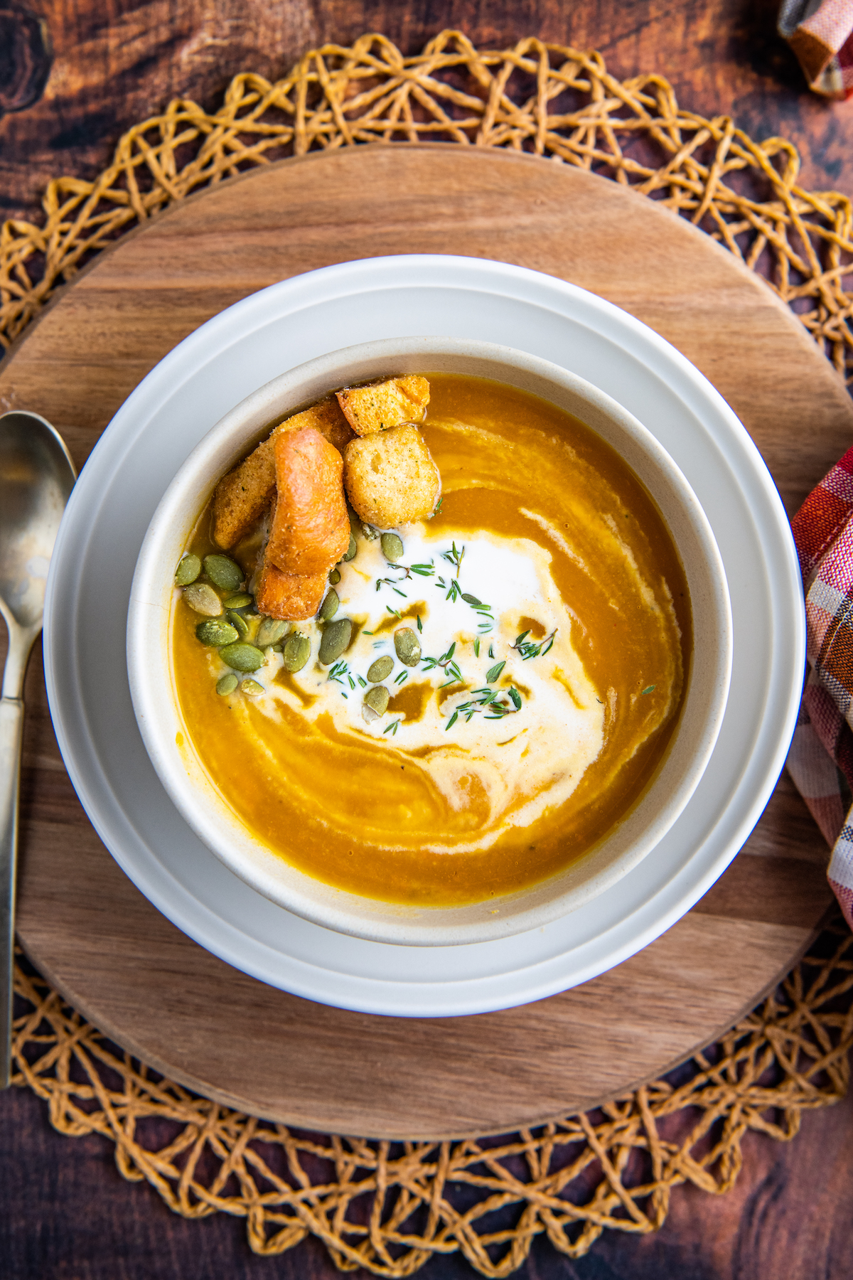 A bowl of butternut squash soup with cream, pumpkin seeds and croutons on top.