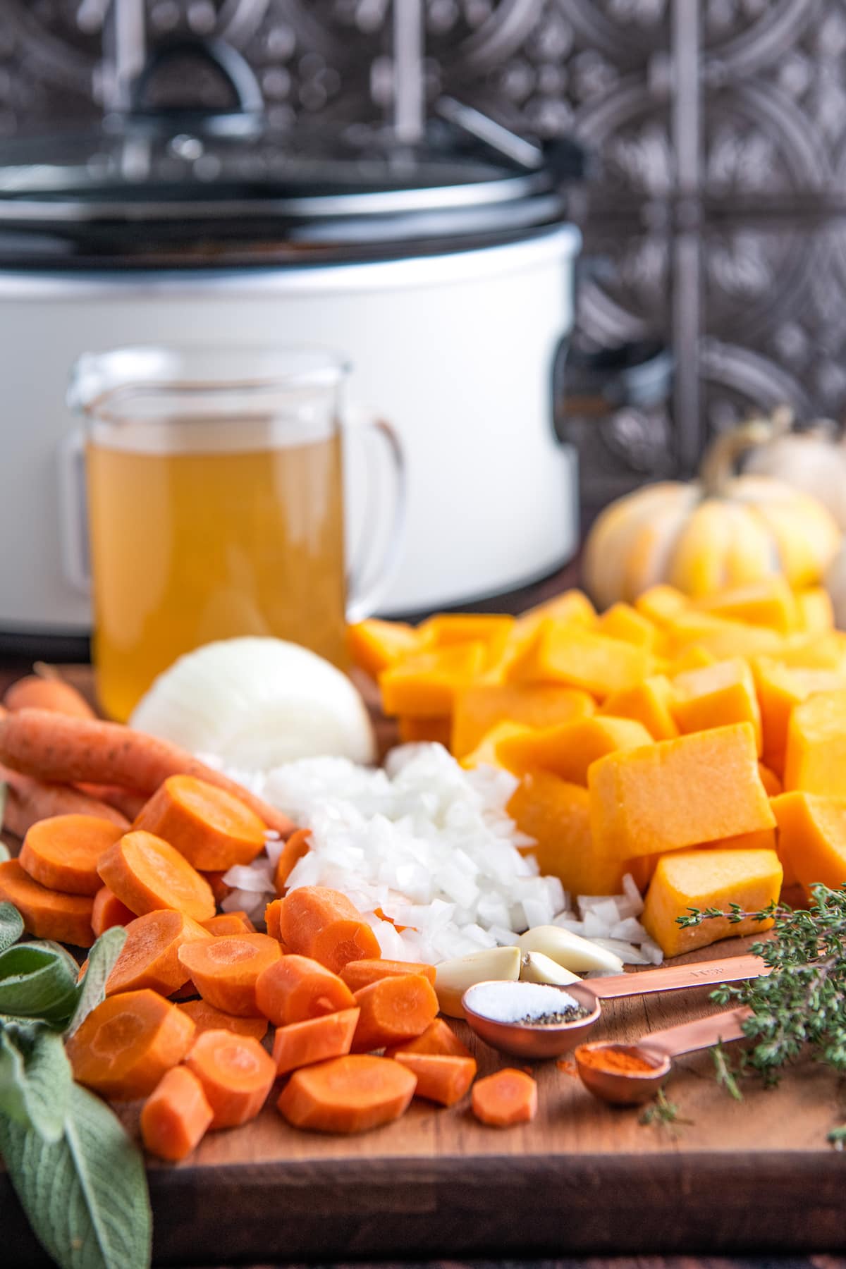 Ingredients for squash soup on a cutting board with a crockpot in the background.