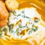A bowl of butternut squash soup with cream on top and thyme.