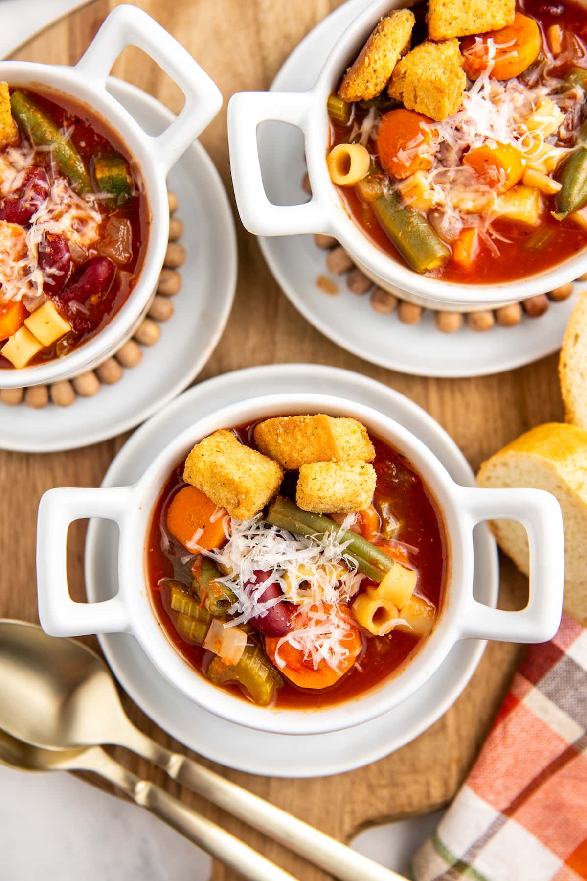 A bowl full of minestrone soup with croutons and parmesan cheese on top.