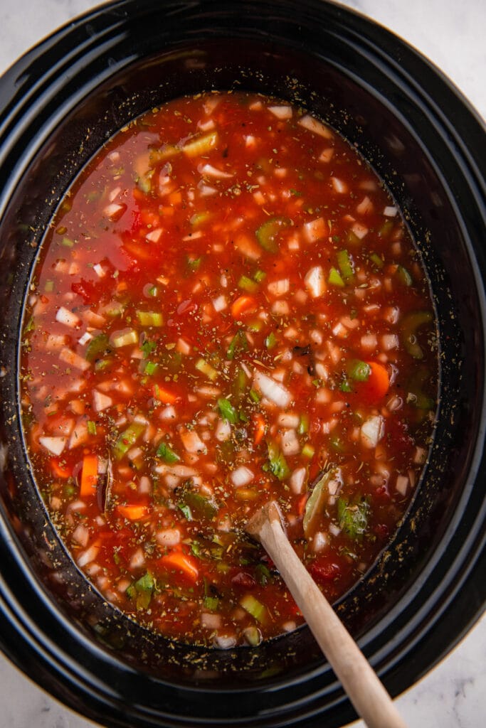 A black crockpot filled with minestrone soup before cooking.