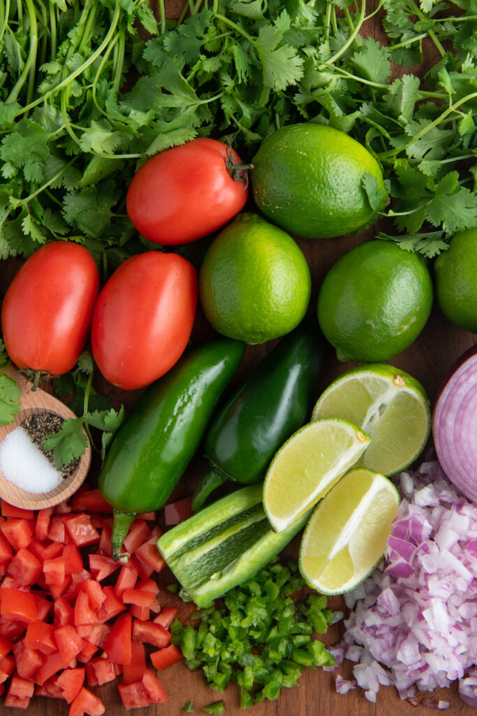 A chopping board filled with vegetables: tomatoes, jalapeño, lime, onion, and cilantro.