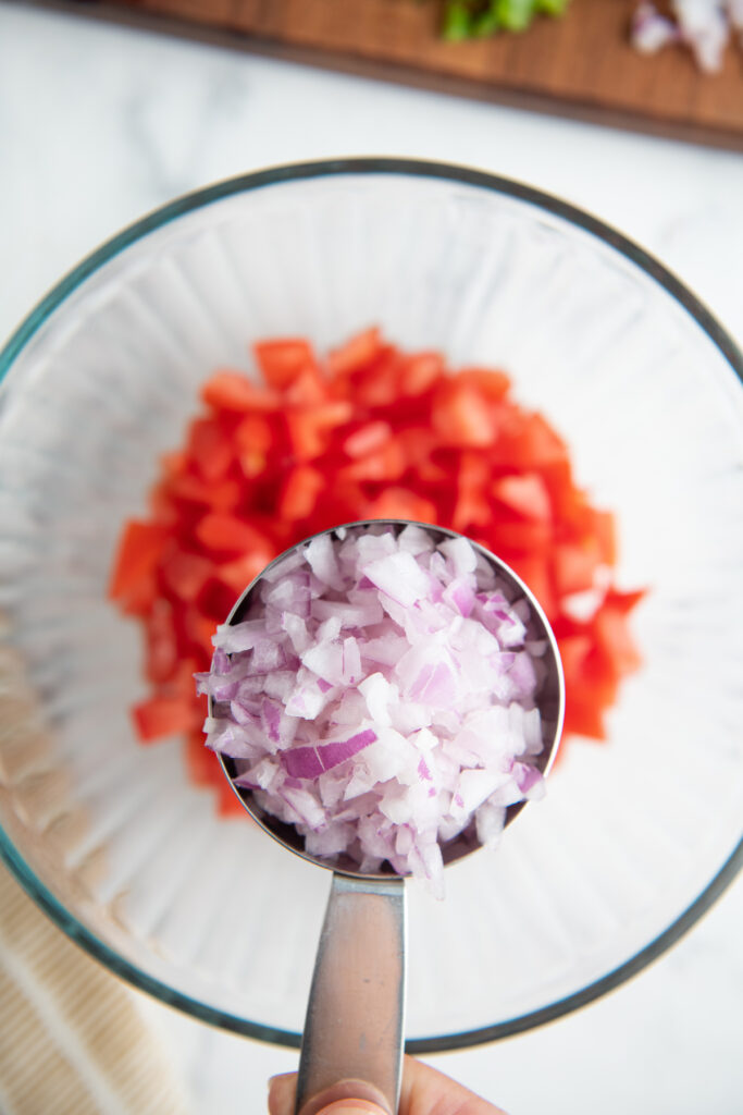 A measuring cup filled with diced red onion over a bowl filled with chopped tomatoes.