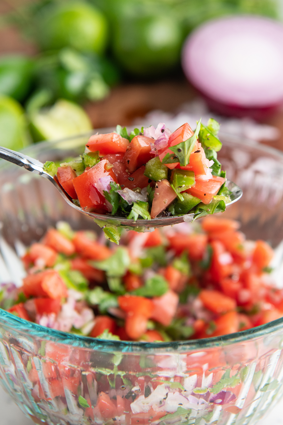 A bowl full of pico de Gallo with a spoon scooping up a spoonful.