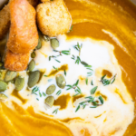 A bowl of butternut squash soup with cream on top.