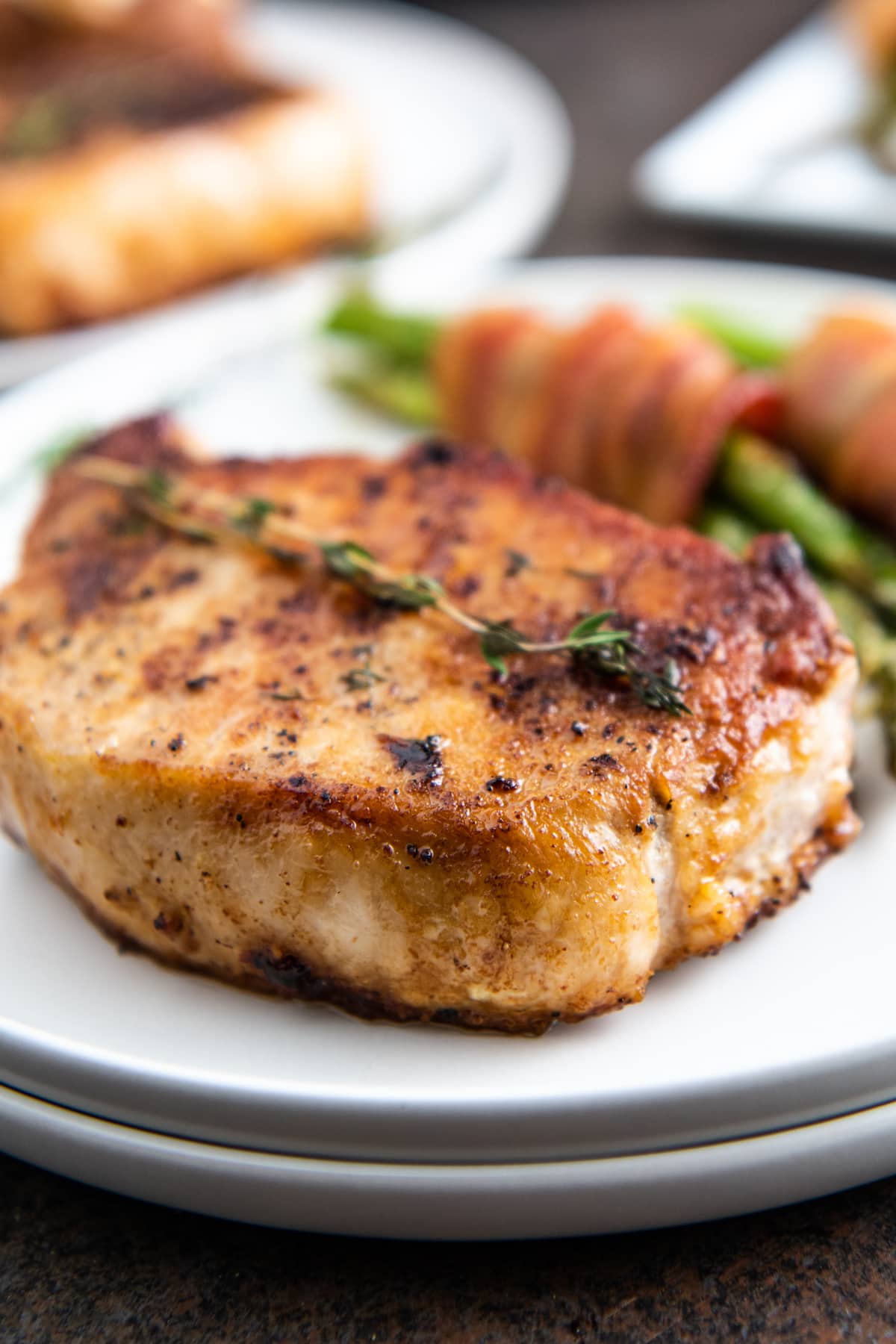 Up close image of a pork chop on a white plate with herbs on top.