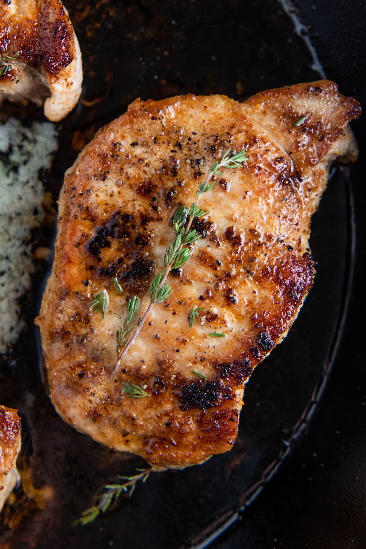 One pork chop in a cast iron skillet with herb butter.