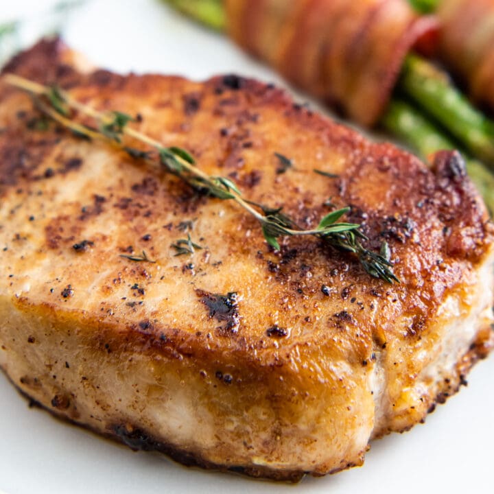 Up close image of a seared pork chop with butter and seasonings.