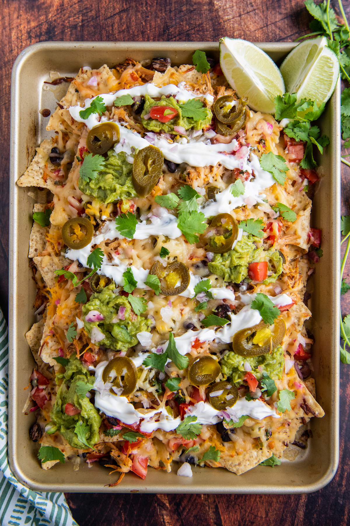 Pork nachos on a baking sheet topped with cilantro, guacamole and sour cream.