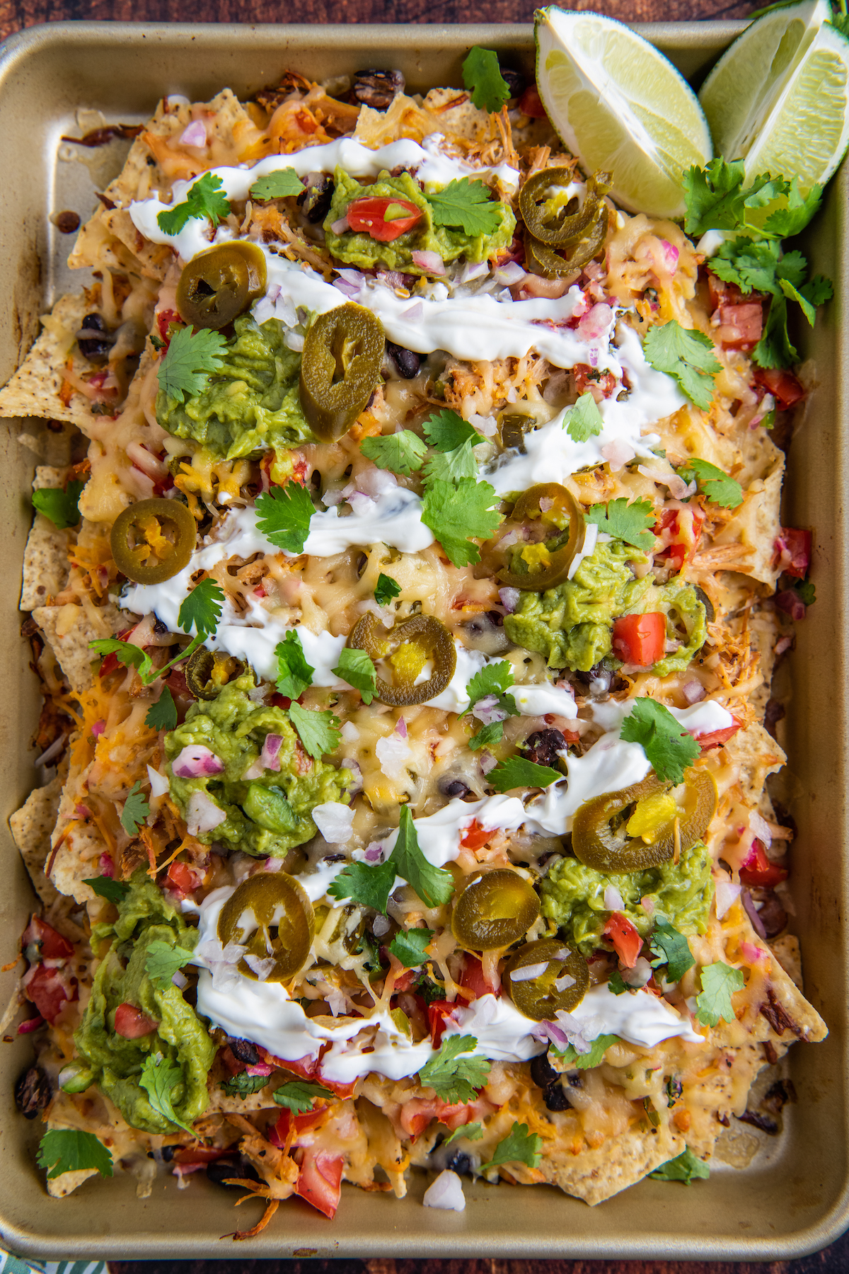 Overhead image of pulled pork nachos on a sheet pan with all the toppings piled on top.