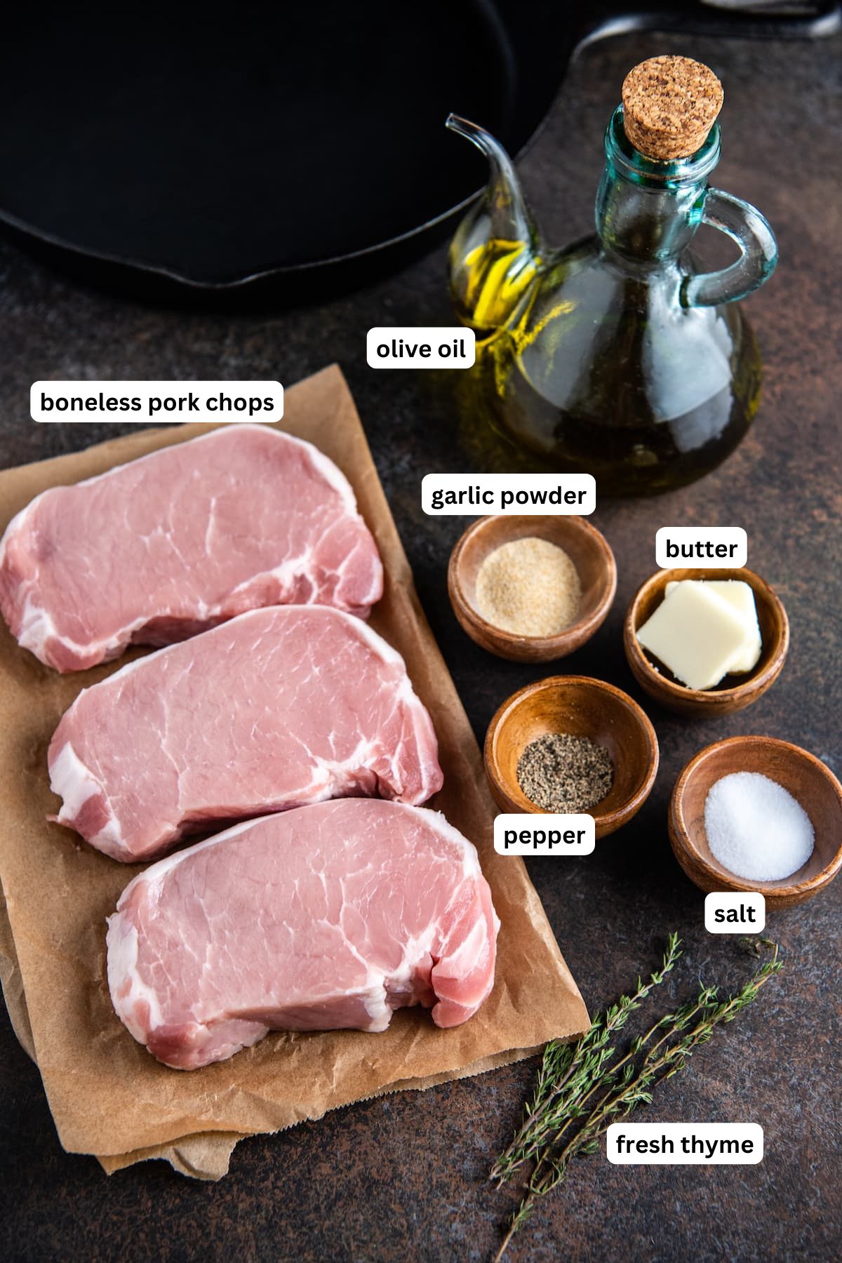 Ingredients for pan fried pork chops recipe in order from top to bottom: boneless pork chops, olive oil, garlic powder, butter, pepper, salt, fresh thyme.