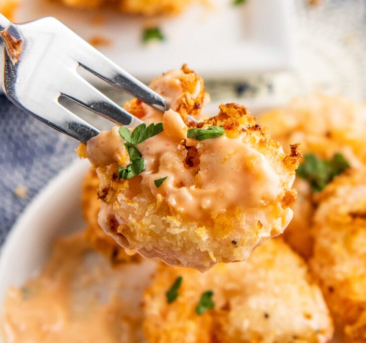 Bang bang shrimp on a plate with a fork picking up one shrimp with sauce on it.