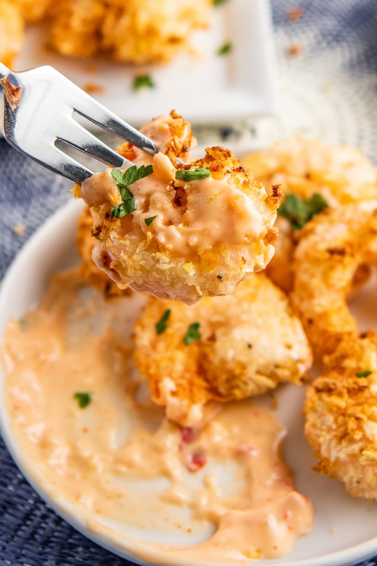 Bang bang shrimp on a plate with a fork picking up one shrimp with sauce on it.