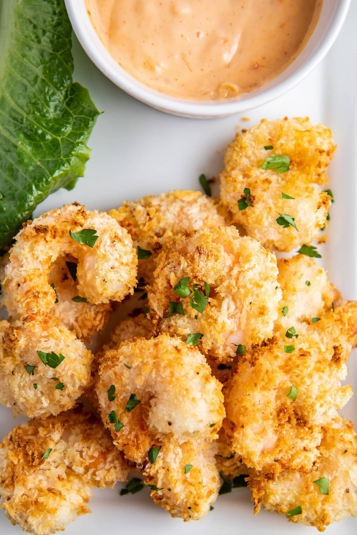 Overhead image of air fried shrimp on a white plate with a bowl of orange sauce.