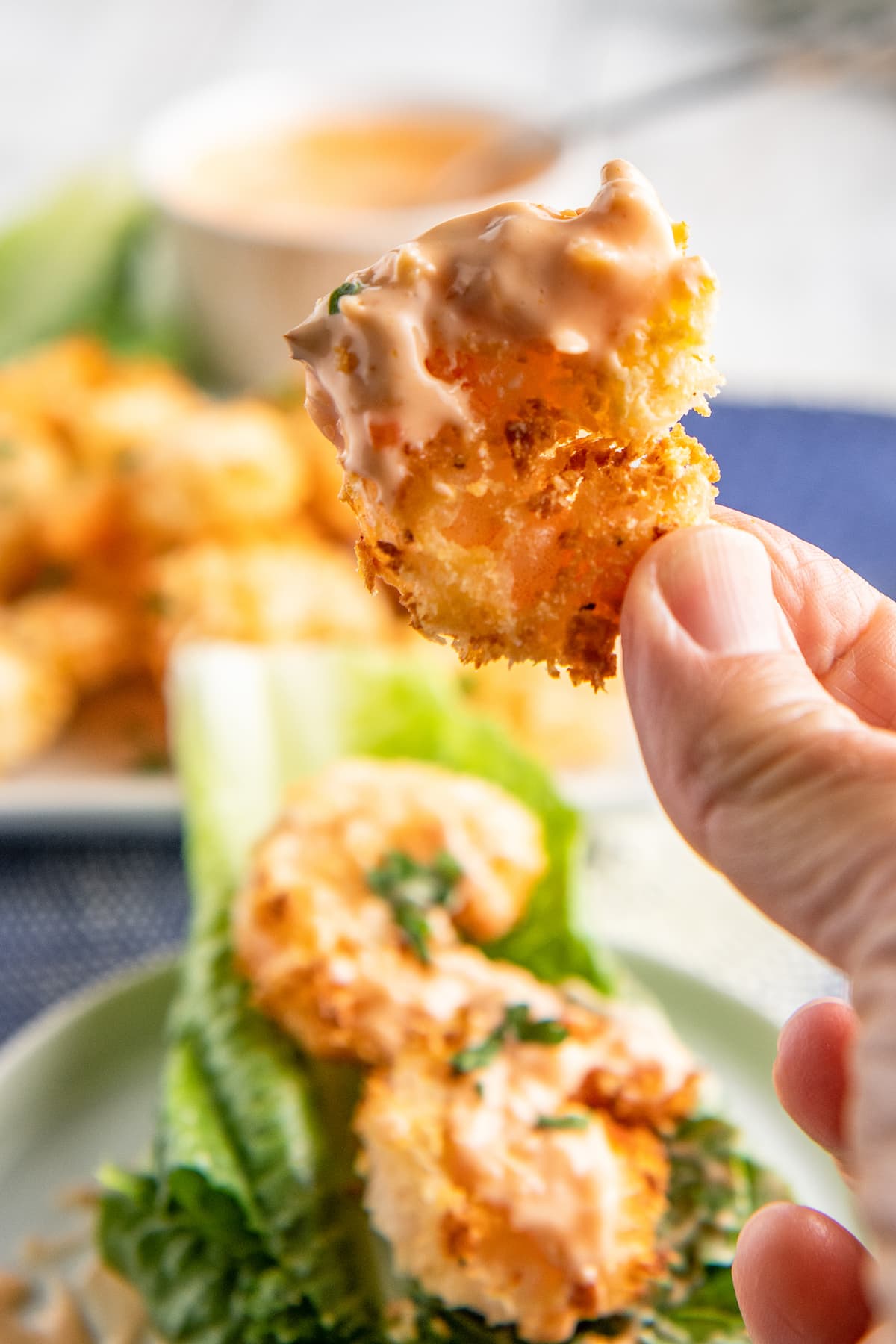 A shrimp with crispy fried coating dipped in orange sauce being picked up.