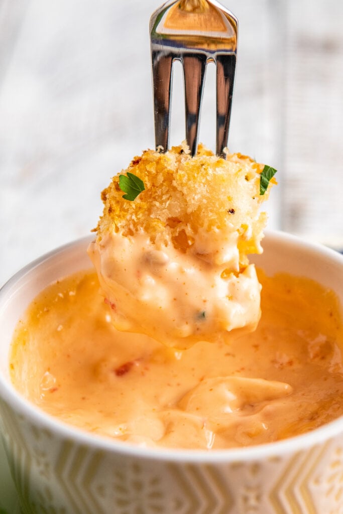 A fried shrimp on a fork being dunked into a bowl of orange sauce.