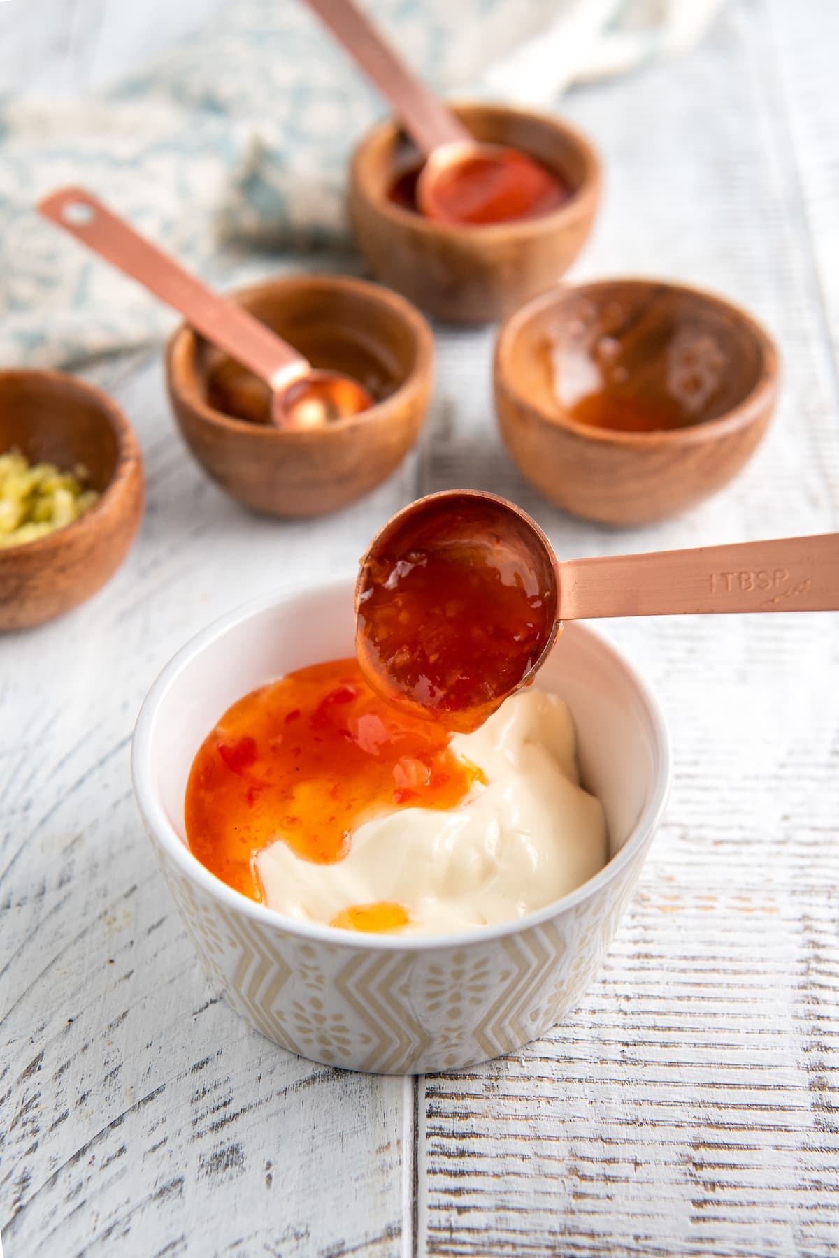 A bowl with mayonnaise with sweet chili sauce being added to it with a spoon.