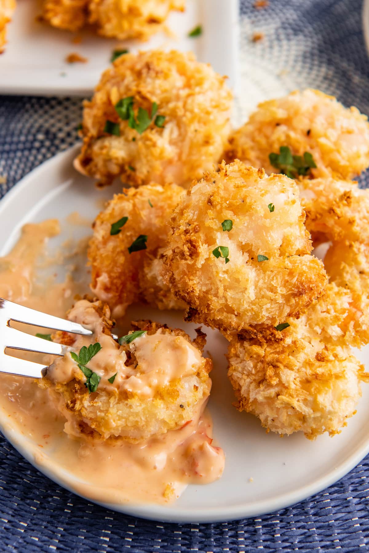 A plate full of fried shrimp being dipped in bang bang sauce.