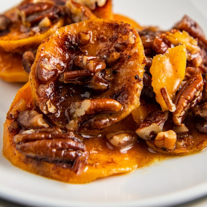 Up close image of candied sweet potatoes with pecans on a white plate.