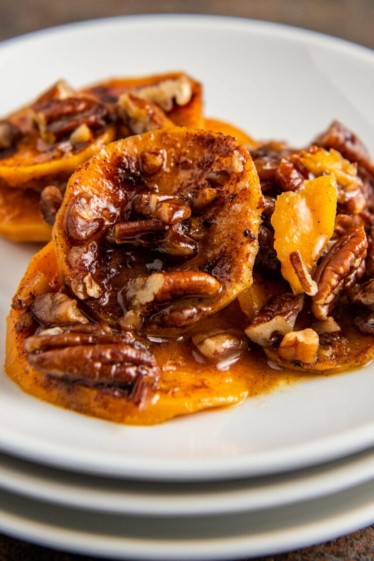 Up close image of candied sweet potatoes with pecans on a white plate.