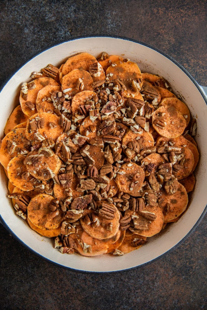 Sliced sweet potato rounds in a baking dish with pecans and seasonings on top.