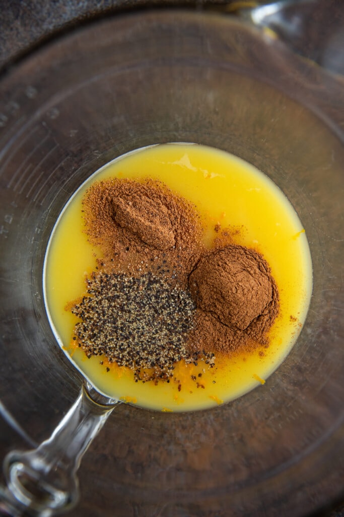 A bowl fill with orange juice with seasonings on top.