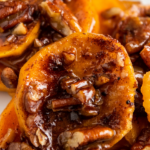 Up close image of candied sweet potatoes on a white plate with pecans.
