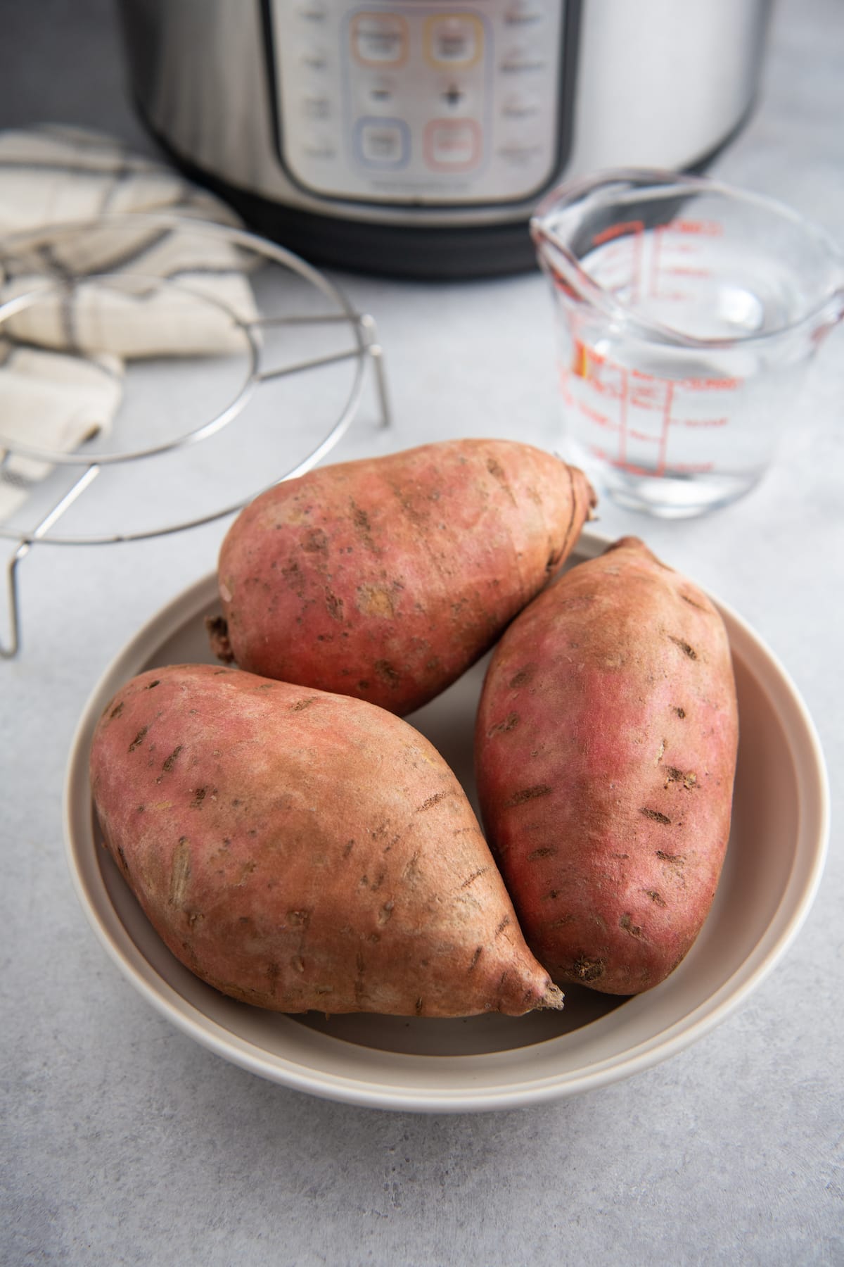Three sweet potatoes on a white plate in front of an instant pot.