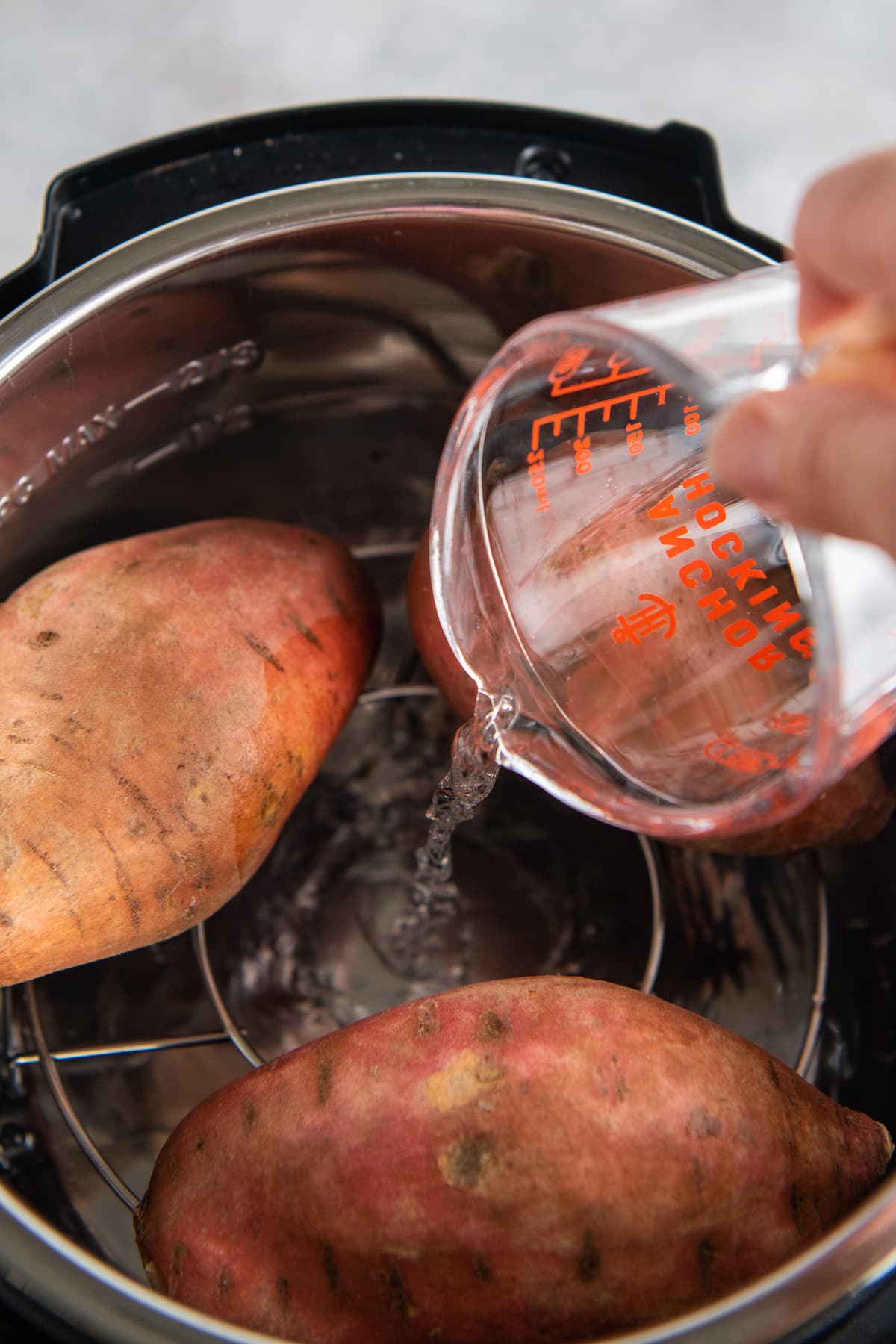 Water being poured into an instant pot with sweet potatoes.