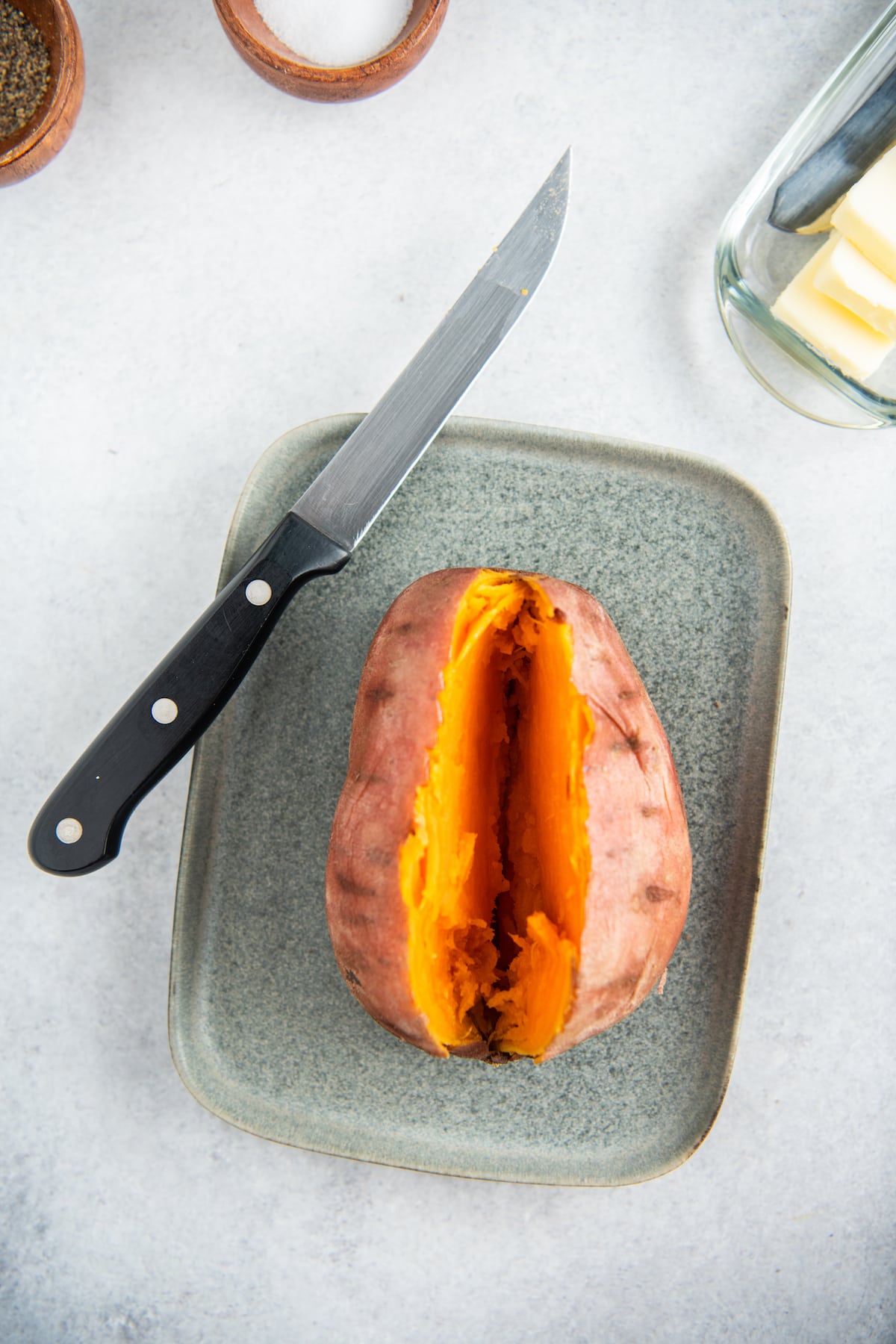 A sweet potato sliced on the center on a plate with a knife.