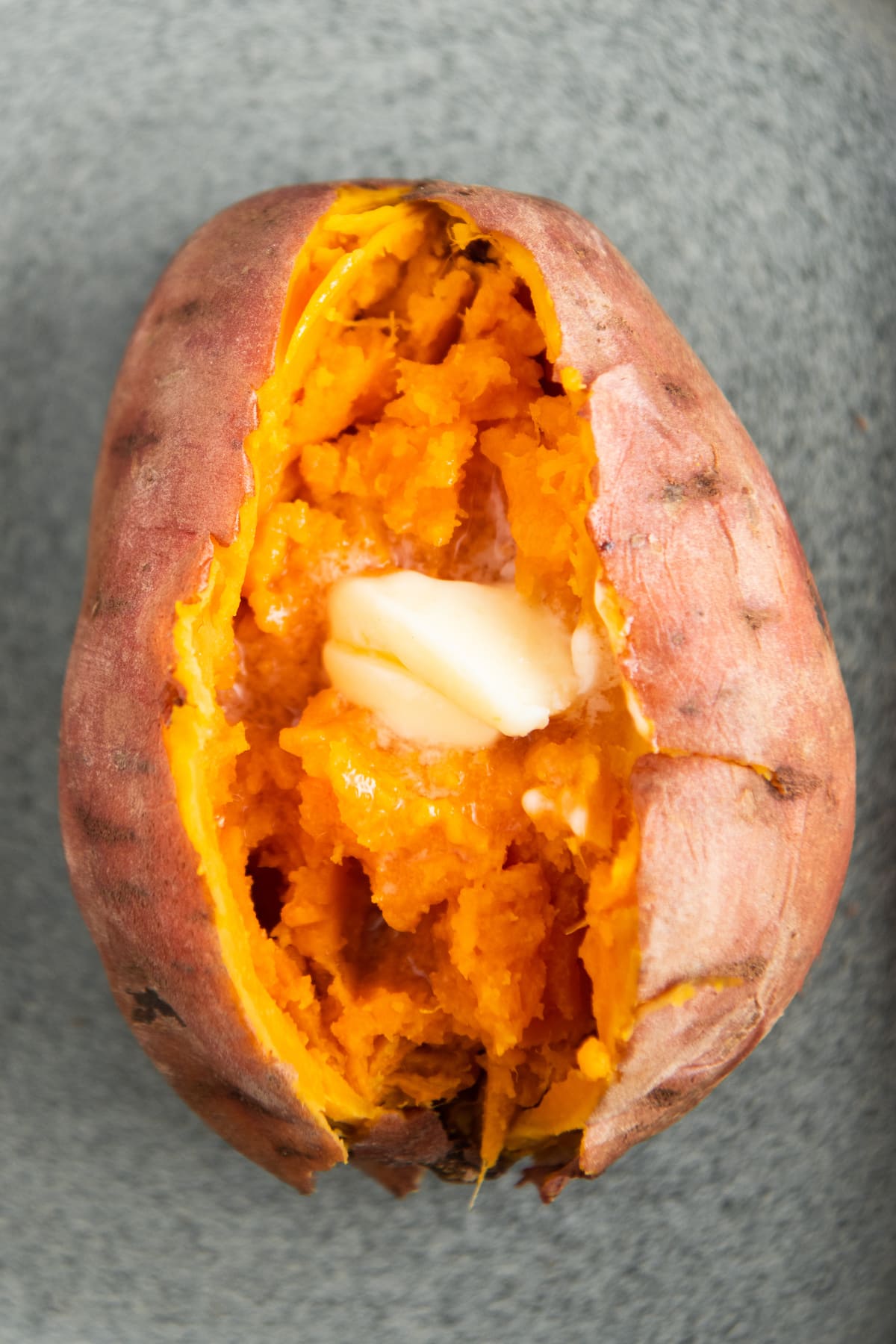 One sweet potato sliced down the center with butter placed inside.