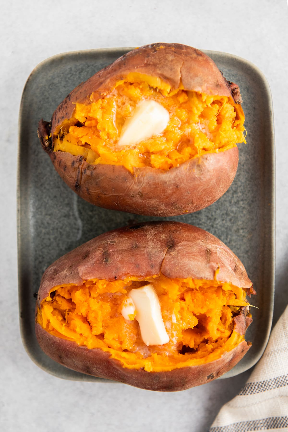 Two sweet potatoes on a plate sliced in half with butter inside.