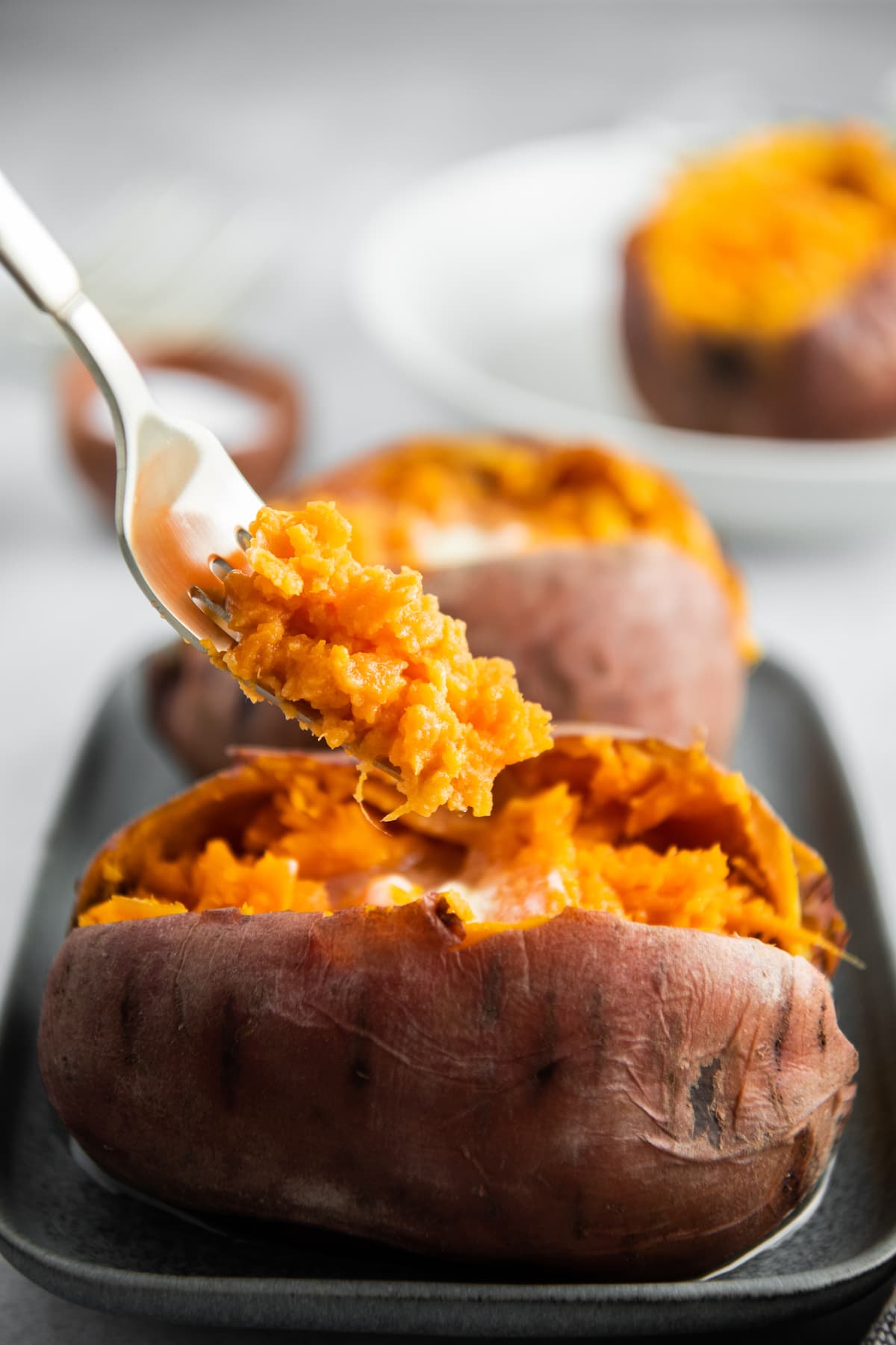 A cooked sweet potato on a plate with a fork scooping out a bite.