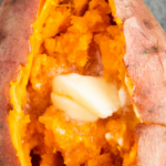 Up close image of a Sweet potato sliced with butter inside on a plate.