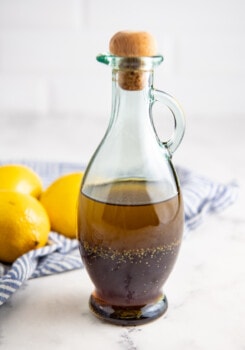 Salad dressing in a glass jar with a lid on top with a tea towel and lemons in the background.