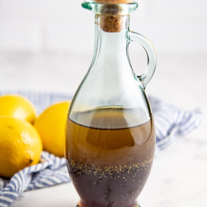 Salad dressing in a glass jar with a lid on top with a tea towel and lemons in the background.