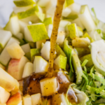 Salad dressing being poured over salad in a bowl.