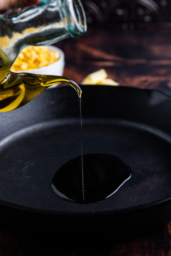 Olive oil being poured into a cast iron skillet.