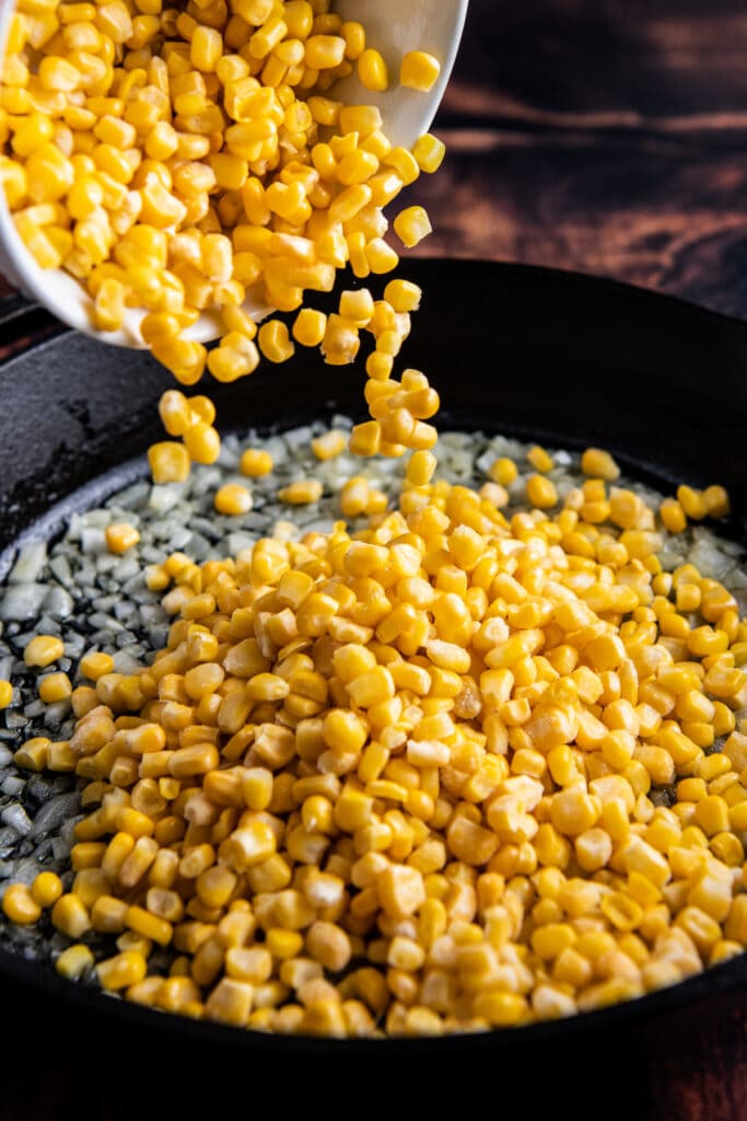 Corn kernels being poured into a cast iron skillet.
