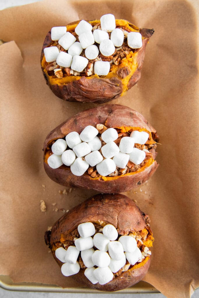Marshmallows piled into the center of sweet potatoes on parchment paper.