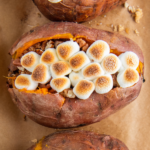 Overhead image of three sweet potatoes stuffed with toasted marshmallows.