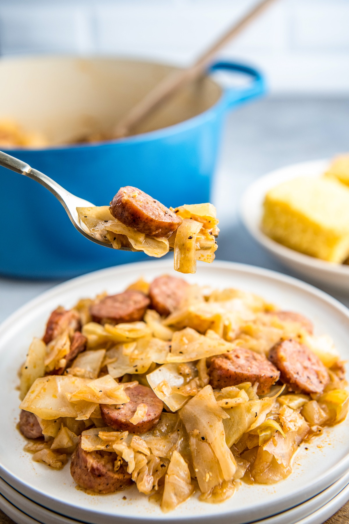 Fried cabbage and sausage on a white plate with a fork picking up a bite.